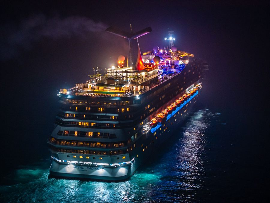 Brightly lit cruise ship sailing at night, seen from above