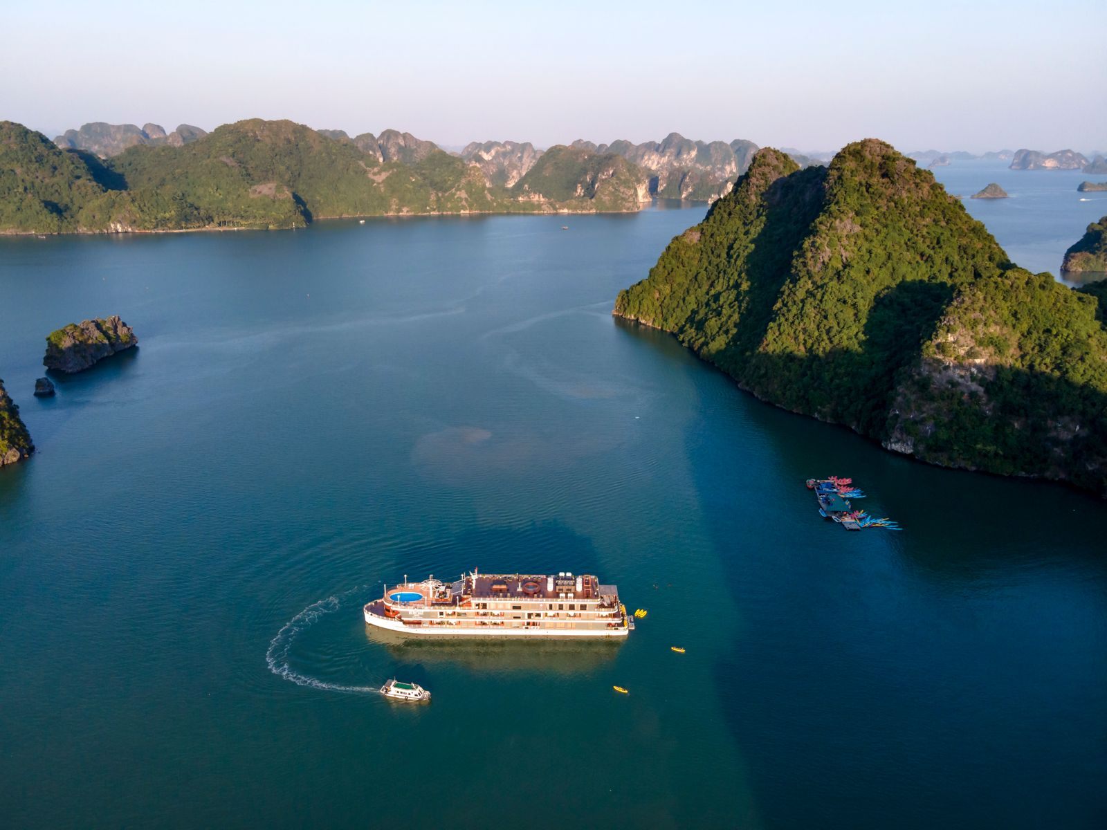 Small cruise ship sailing between limestone islands in a green bay